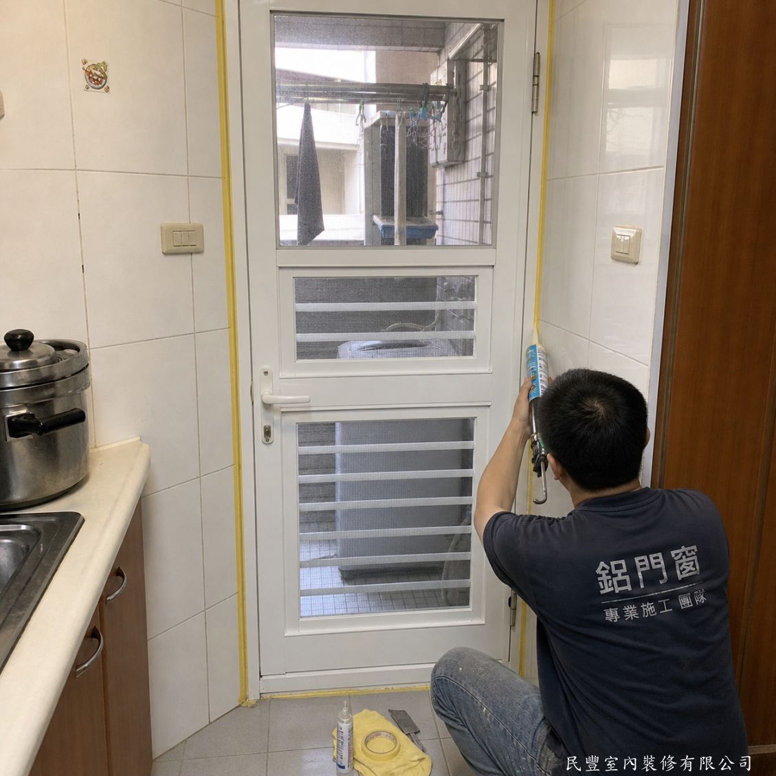 民豐室內裝修-廚房後陽台舊鋁門更換三合一通風門-門框固定完成後，師傅以美紋膠帶保護周邊磁磚，再施打防水矽利康對門框四周縫隙進行密封收邊，有效防止雨水及蟲蚊從縫隙進入室內